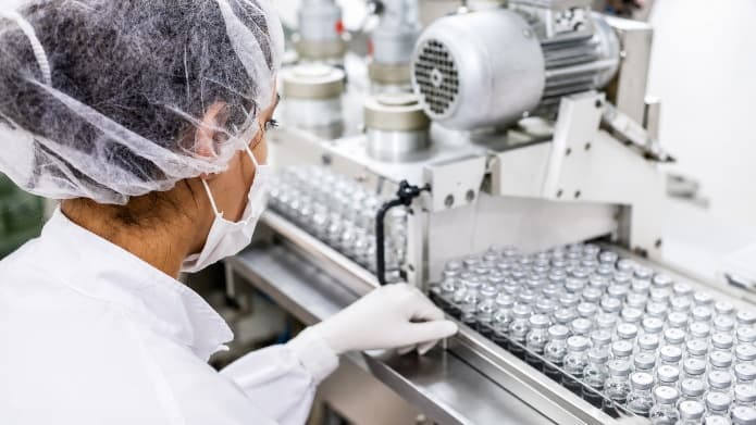Pharmacy technician in protective attire inspecting vials on a production line